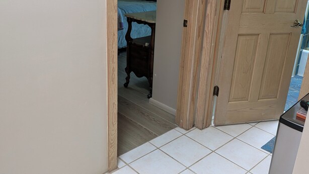 Un pasillo con suelo de baldosas que conduce a un dormitorio con cama y mesita de noche.