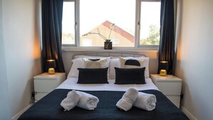 Ein ordentlich bezogenes Bett mit zwei Kissen, einer Nachttischlampe und einem Fenster mit Vorhängen.