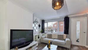 Ein modernes Wohnzimmer mit Flachbildfernseher, einer Couch, einem Couchtisch und einem Fenster mit Vorhängen.