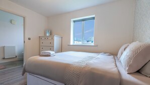 Un dormitorio con cama, cómoda, ventana y radiador.