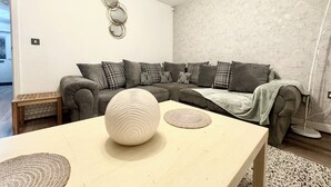 Una sala de estar moderna con un sofá seccional gris, un jarrón blanco redondo y una mesa de centro de madera.