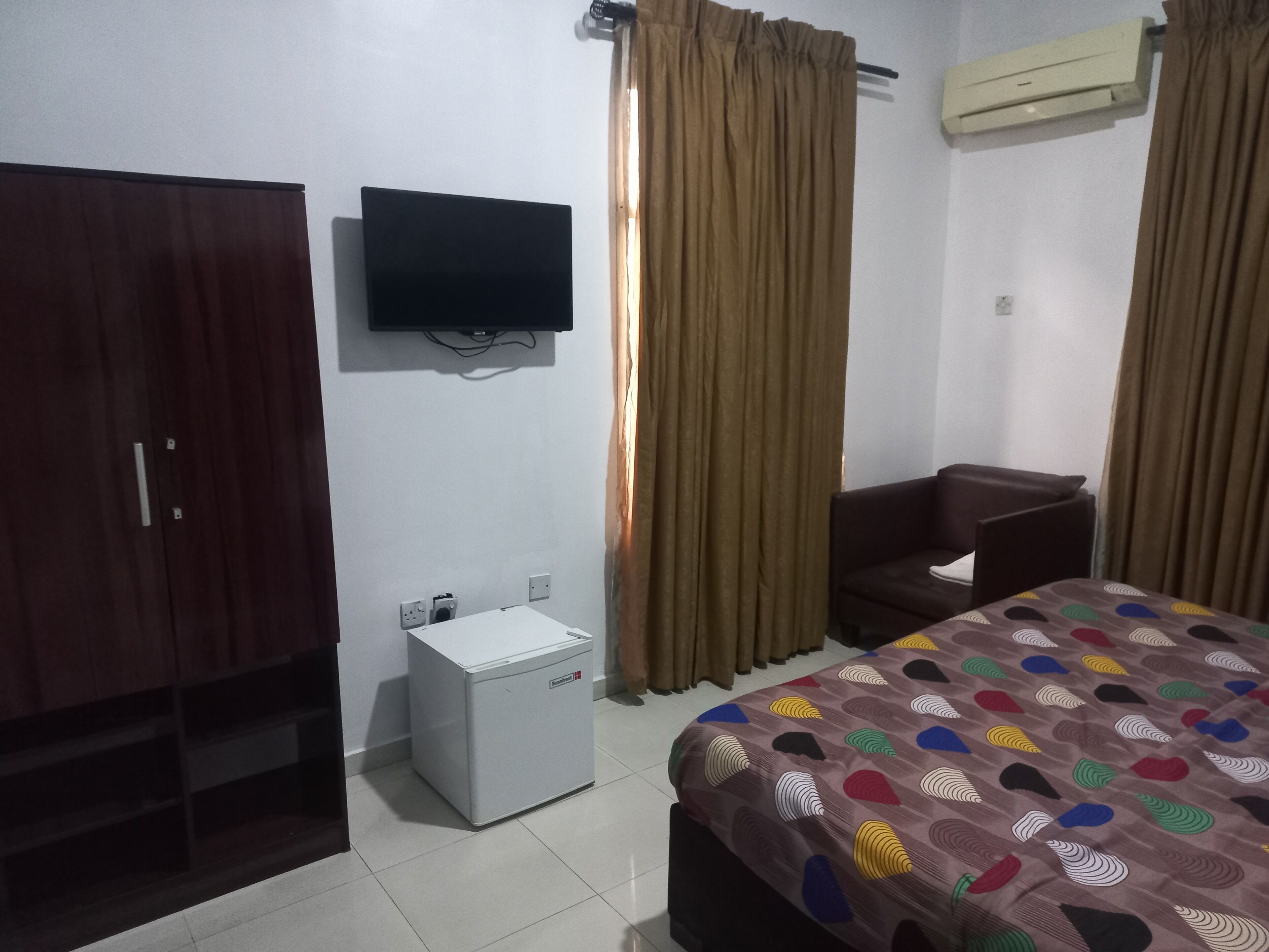 A hotel room with a bed, a desk, a wardrobe, a television, and an air conditioner.