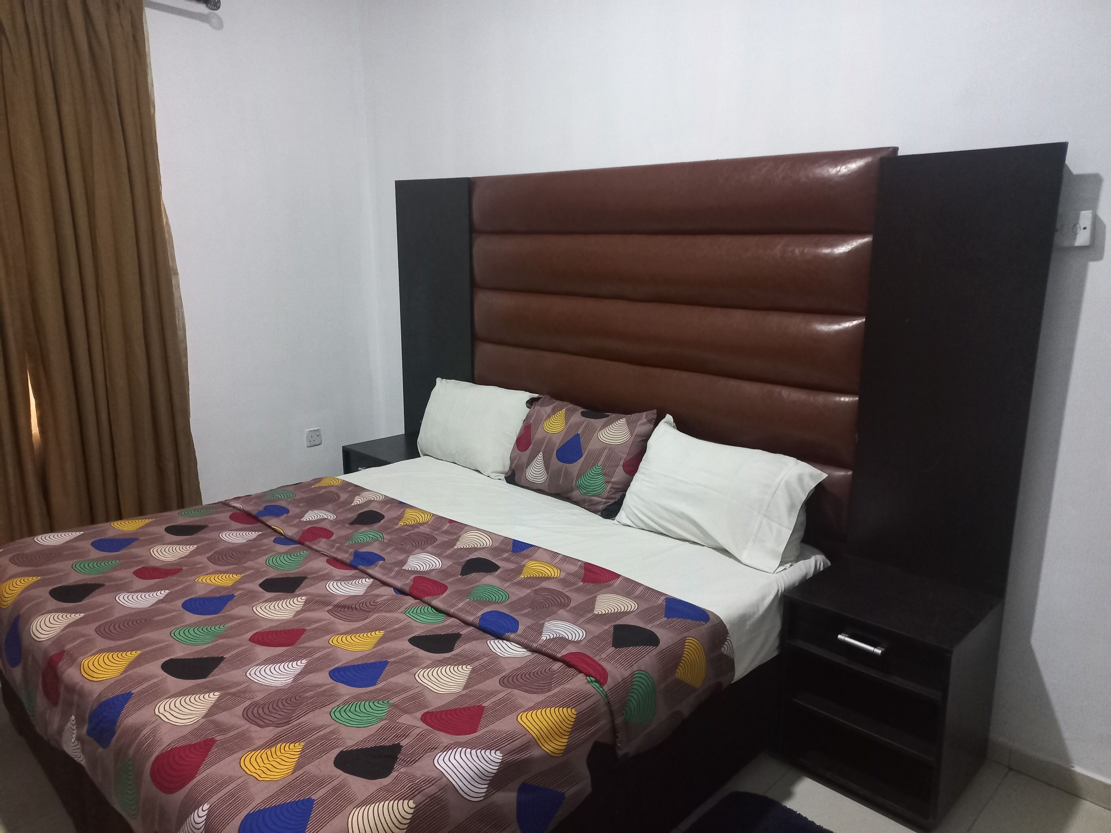 Een hotelkamer met een bed, nachtkastje, bruin hoofdeinde en een bed met een patroon.