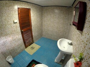 Een kleine badkamer met een blauwe betegelde vloer, een houten deur, een witte wastafel en een spiegel.
