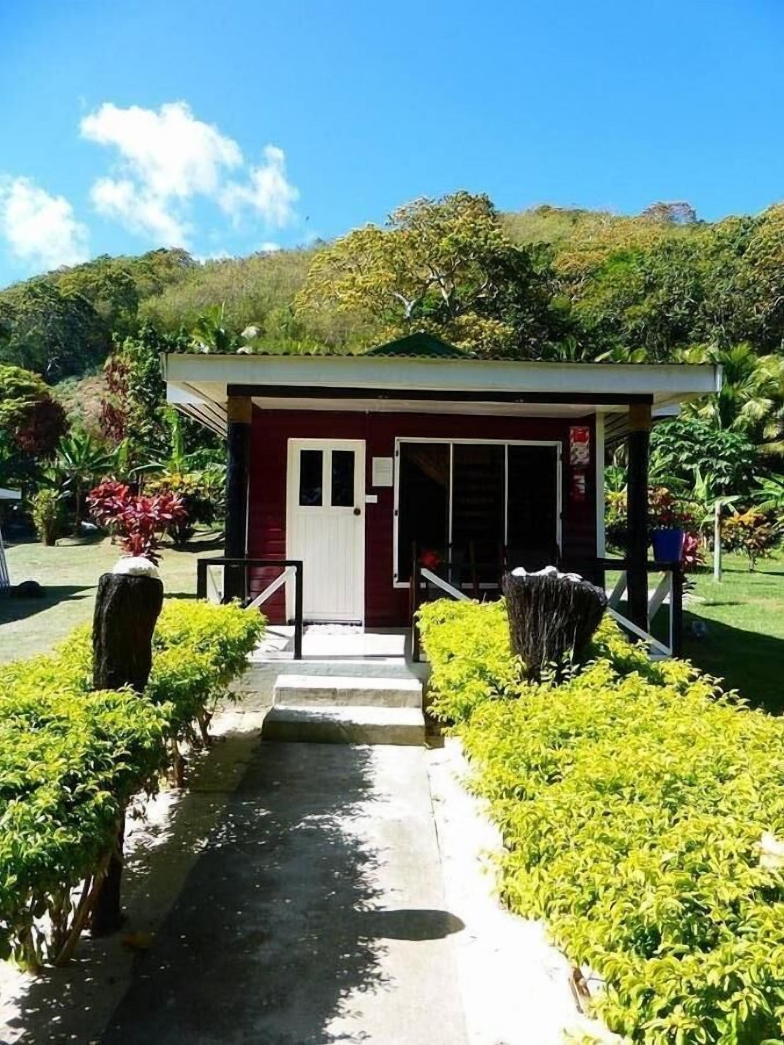 A small, red building with a white door, surrounded by well-maintained greenery and a clear sky.