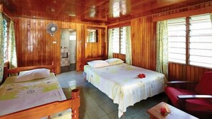 Een houten kamer met twee bedden, een rode stoel en een ventilator.