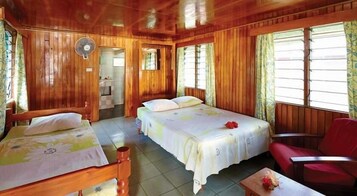 Una habitación de cabaña de madera con dos camas, una silla roja y un ventilador.
