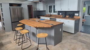 Una cocina moderna con una isla central, taburetes de bar, electrodomésticos de acero inoxidable y un amplio ventanal.
