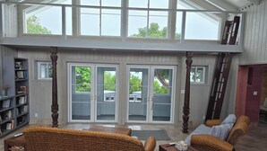 Amplia sala de estar con techo alto, ventanas grandes y puertas de vidrio correderas que dan a un patio exterior.