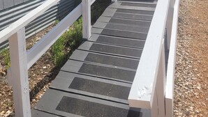Eine überdachte Außentreppe führt zu einem Haus mit weißem Geländer und einer Veranda.