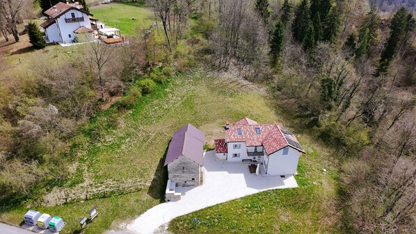 An aerial view of a house with a red-tiled roof, surrounded by a grassy area and trees.