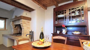 A wooden dining table with a bottle of Prosecco and glasses, a brick fireplace, and a wooden cabinet with glass doors.