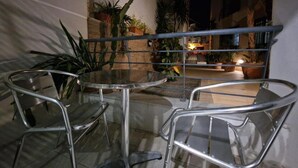 A glass-top table with four metal chairs in an outdoor patio area with potted plants and a railing. - Bugibba Central Modern Apartment, Charming 2-bedroom apartment with AC,  WiFi  (San Pawl il-Baħar)