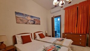 A hotel room with two beds, a painting on the wall, and a view of the outdoors. - Bugibba Central Modern Apartment, Charming 2-bedroom apartment with AC,  WiFi  (San Pawl il-Baħar)