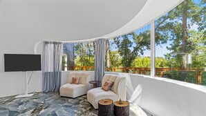 A modern living room with two sofas, a TV, and a large window overlooking a wooden deck. - The Fairy House | 3 Beds 2 Baths (Elgin)