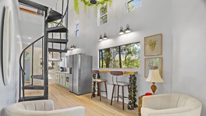 A modern kitchen with a central island, a spiral staircase, and a dining area with two chairs. - The Fairy House | 3 Beds 2 Baths (Elgin)