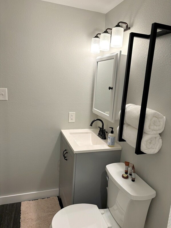 Une salle de bain avec un lavabo blanc, un miroir et des toilettes. Des serviettes sont accrochées au mur et des articles de toilette sont posés sur le lavabo.