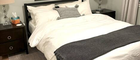 A neatly made bed with white and gray bedding, two bedside tables with lamps, and a framed sign above the bed.