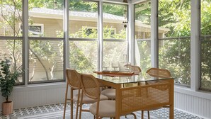 Une véranda avec une table en verre et des chaises en osier, de grandes fenêtres et une plante en pot.