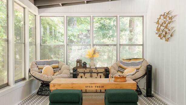 Une pièce chaleureuse avec une grande fenêtre, une table en bois portant l’inscription « produits sortis du four », deux fauteuils verts et un élément décoratif mural.