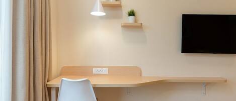 A modern room with a desk, chair, mounted TV, and wall-mounted shelves with plants.