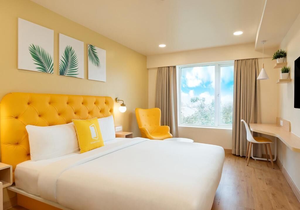 A hotel room with a large bed, a desk, a chair, a window with curtains, and wall art.