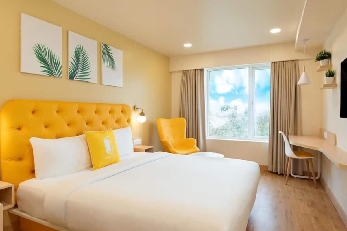 A hotel room with a large bed, a desk, a chair, a window with curtains, and wall art.