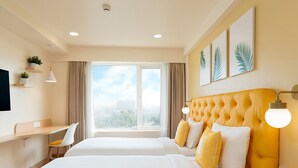 A hotel room with two beds, a desk, a chair, a TV, a phone, and a window with a city view. - Bloom Hotel SG Highway (Ahmedabad)
