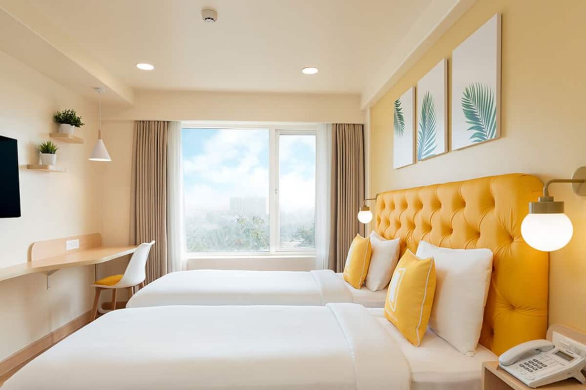 A hotel room with two beds, a desk, a chair, a TV, a phone, and a window with a city view.
