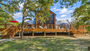 A modern house with a wooden deck, a glass dome structure, and a staircase. - The Bird House | 6 Beds 2 Baths (Bastrop County)