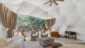 A tented room with a large window, two sofas, a wooden table, and a ceiling fan. - The Bird House | 6 Beds 2 Baths (Bastrop County)