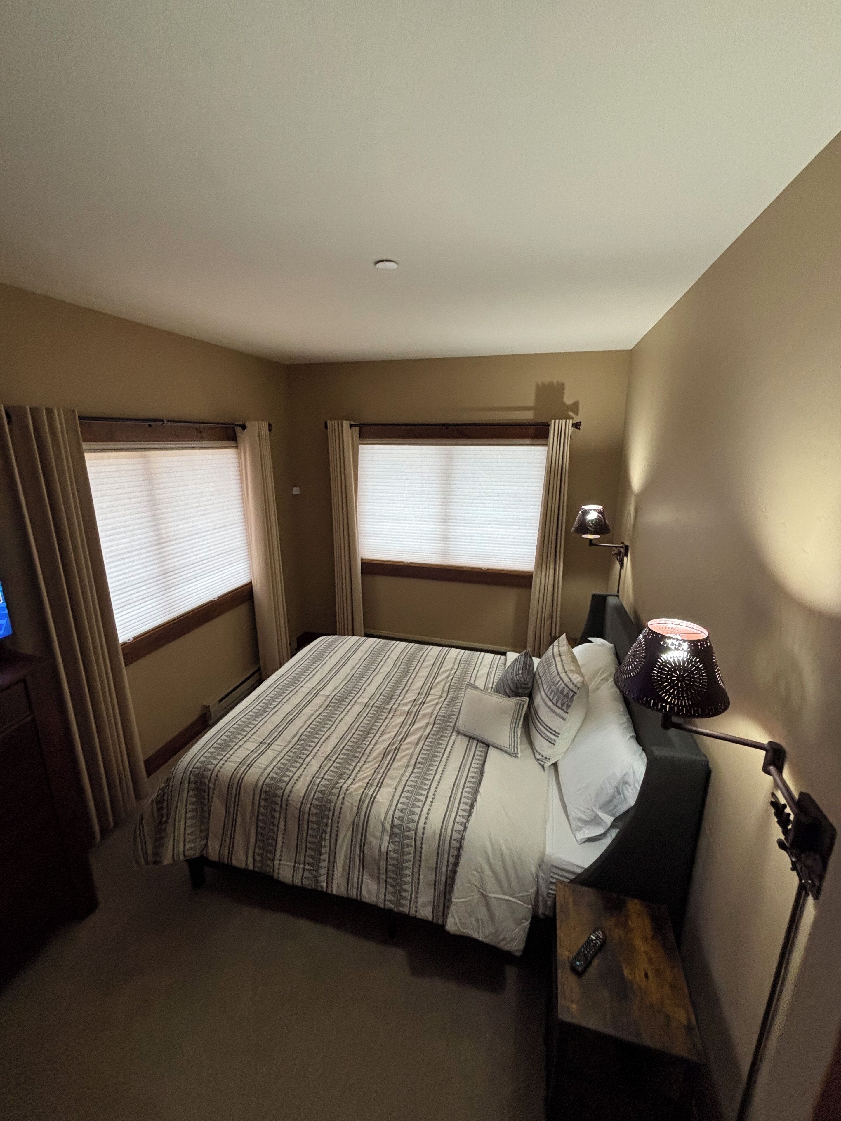 Una habitación de hotel con cama, cortinas, lámpara y televisor.