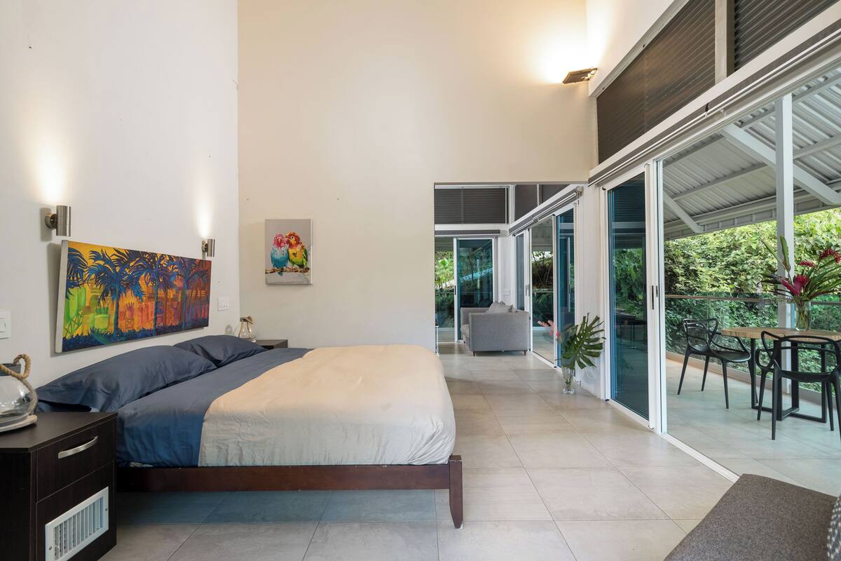 Ein modernes Schlafzimmer mit einem großen Bett, einem Gemälde und Blick auf einen Balkon mit Gartenmöbeln.