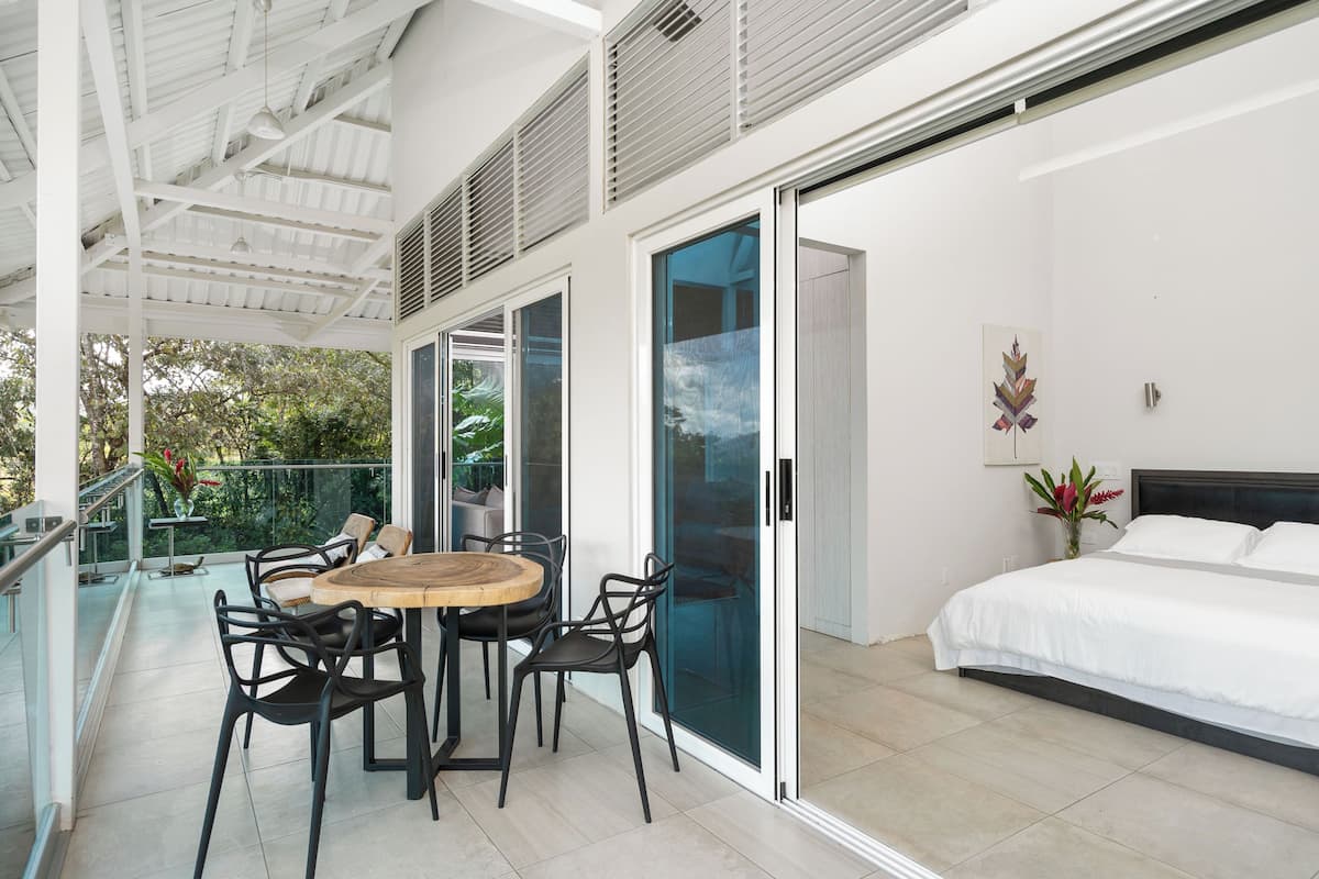 Ein modernes Schlafzimmer mit einem großen Bett, einem Balkon mit Essbereich und einer Glastür, die in einen Garten führt.