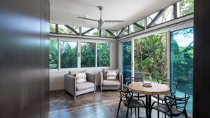 A conservatory with a ceiling fan, large windows, and a round wooden table with chairs. - Casa Maracuya (San Mateo)