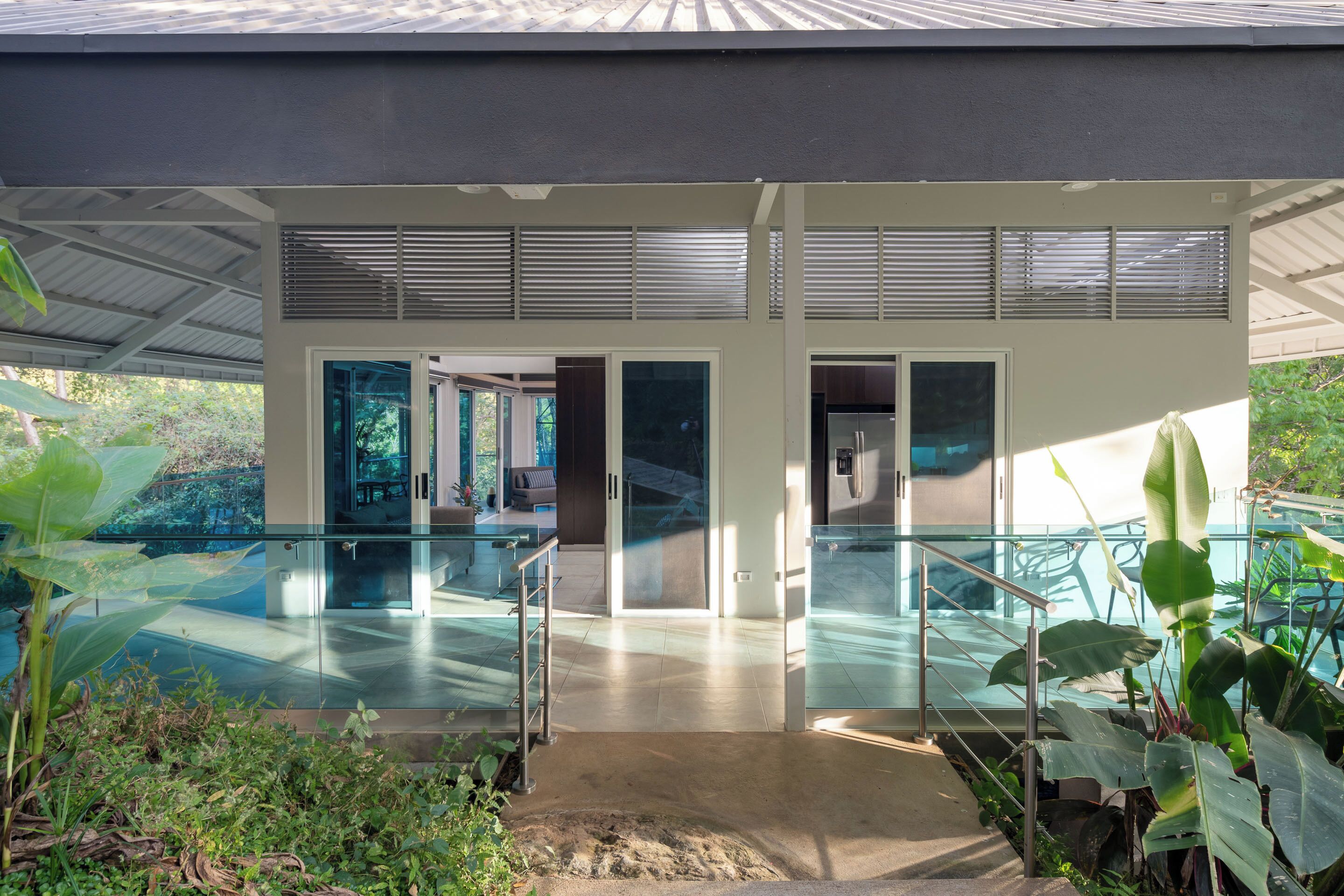 Uma casa moderna com um pátio envidraçado, uma escadaria e vista para o verde ao redor.