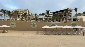 A beach with sun loungers and umbrellas, palm trees, and a building with a starfish mural. - Luxury suite in serene San José del Cabo with AC, WiFi (San José del Cabo)