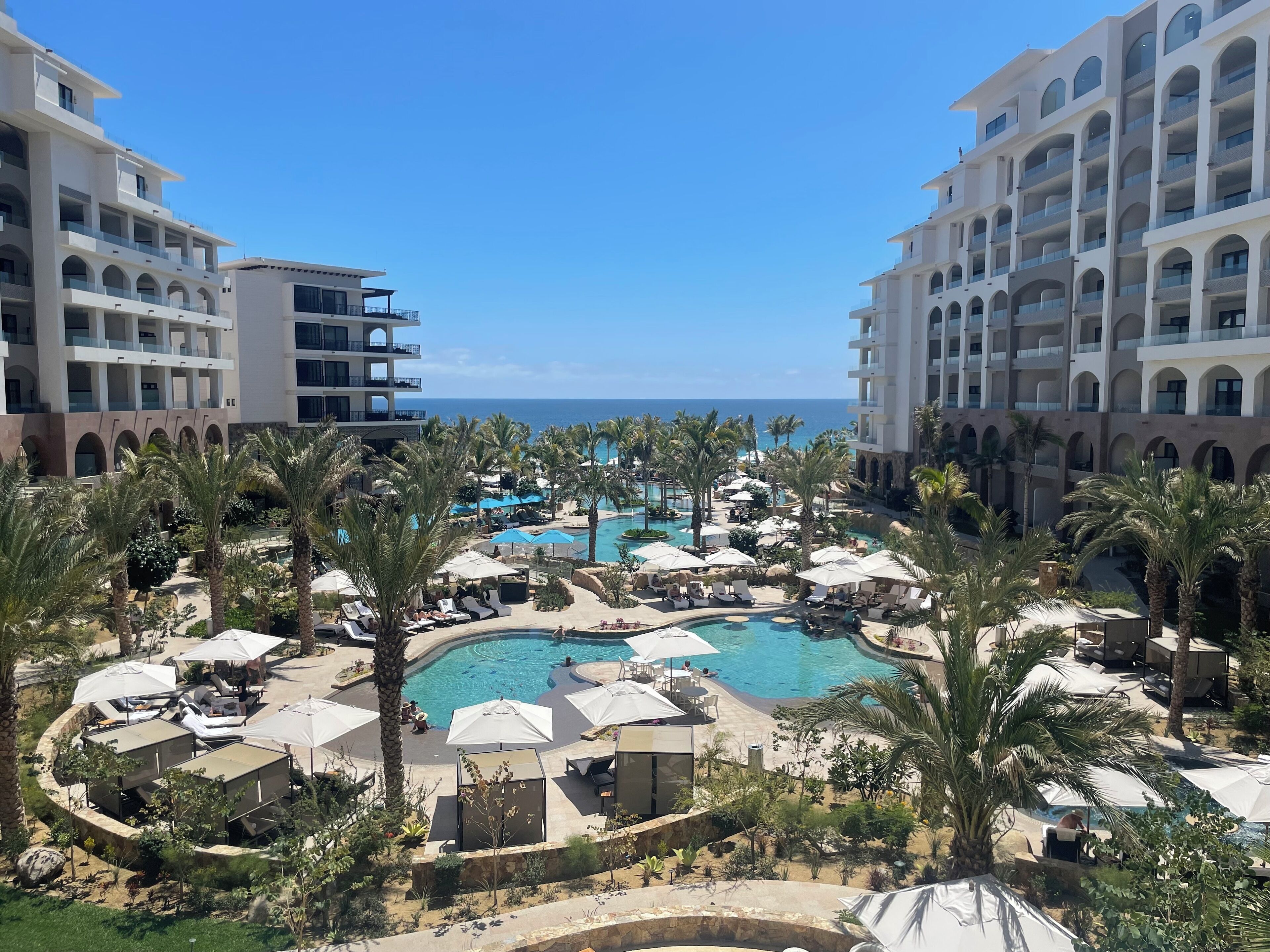 A resort with a central pool, palm trees, and a view of the sea.