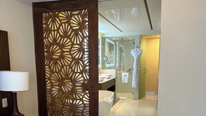 A hotel room with a bed, a wooden partition, a bathroom with a glass door, and a robe hanging on a hook. - Luxury suite in serene San José del Cabo with AC, WiFi (San José del Cabo)