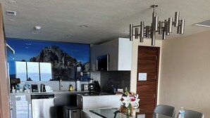 A modern kitchen with a glass dining table, grey chairs, and a view of the sea through a large window. - Luxury suite in serene San José del Cabo with AC, WiFi (San José del Cabo)