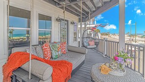 A covered outdoor seating area with a view of the beach, a hanging chair, and a small round table with a vase of flowers. - Ocean Lakes A9 – Huge Decks, Swings, and the Beach Just Steps Away! (Myrtle Beach)