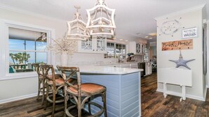 A kitchen with a large island, wooden chairs, a chandelier, and a view of the ocean. - Ocean Lakes A9 – Huge Decks, Swings, and the Beach Just Steps Away! (Myrtle Beach)