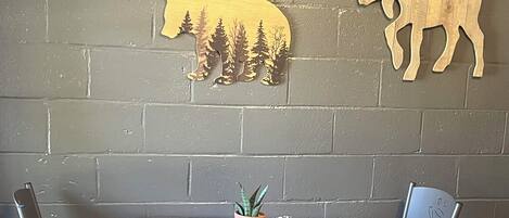 A dining area with a table and two chairs, a potted plant, and two wooden animal wall decorations.