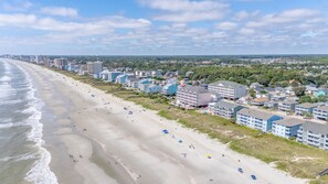 Une zone hôtelière située sur la côte, avec un accès direct à la plage, des bâtiments à plusieurs étages et une plage de sable dotée de parasols.