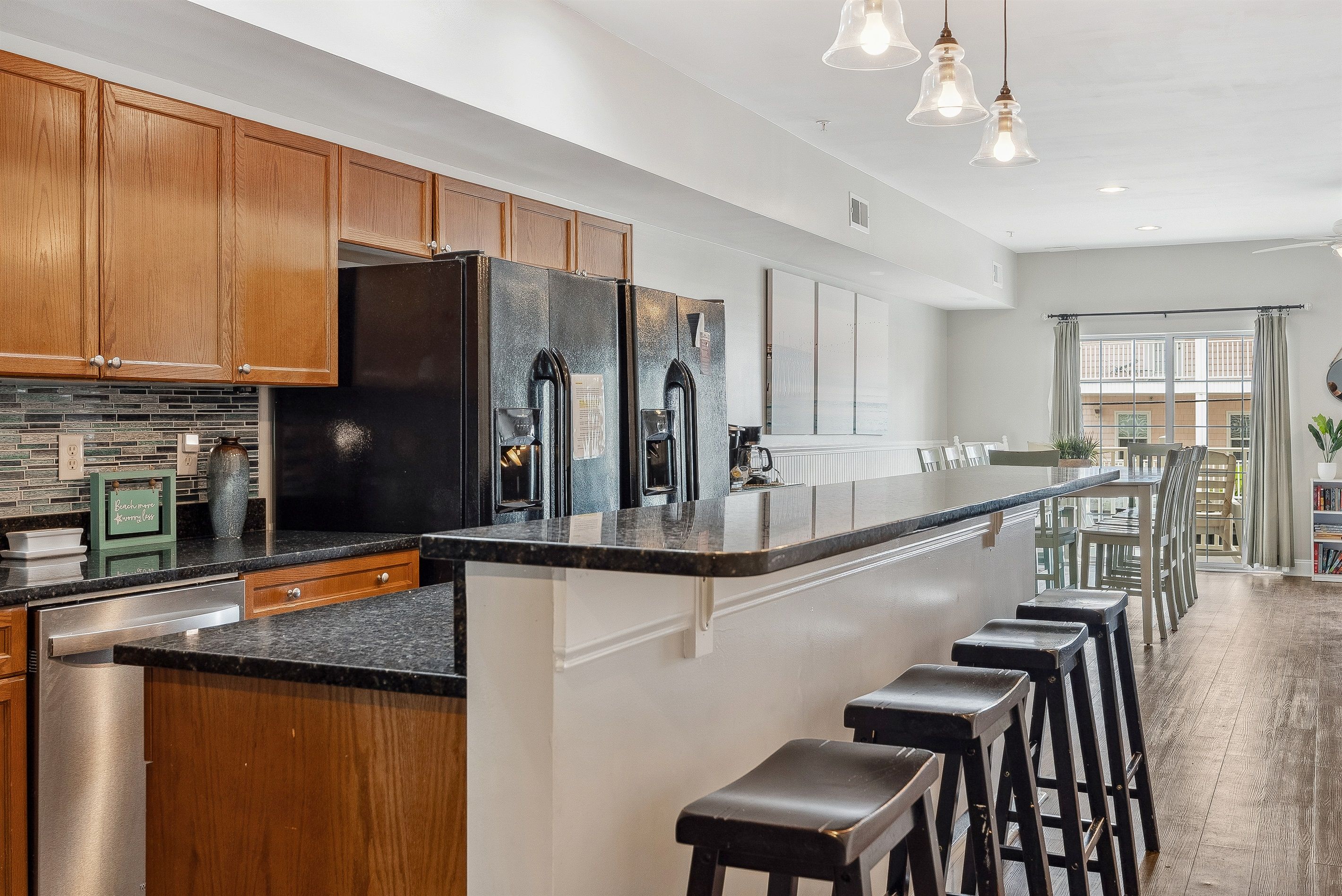 A modern kitchen with wooden cabinets, a large black refrigerator, a central island with bar stools, and a view to a dining area.