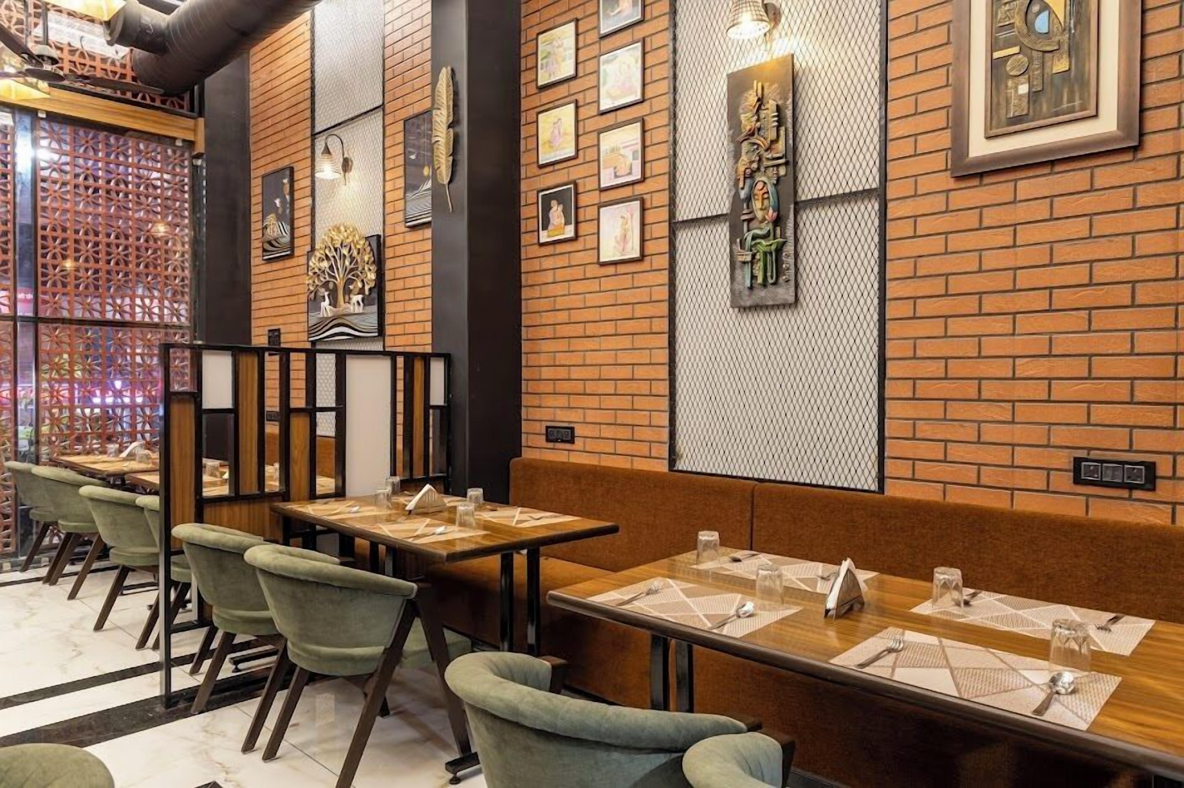 En restaurant med murstensvægge, indrammede kunstværker og grønne polstrede stole.