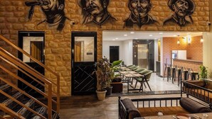 A lobby with a stone wall mural, a staircase, and a seating area with tables and chairs. - Hotel Money Plant (Chhatrapati Sambhajinagar)