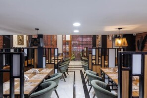 A modern restaurant with a central aisle, green upholstered chairs, and a patterned floor. - Hotel Money Plant (Chhatrapati Sambhajinagar)