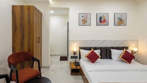 A hotel room with a bed, two bedside lamps, a nightstand, a wooden wardrobe, a red chair, and three wall-mounted artworks. - Hotel Money Plant (Chhatrapati Sambhajinagar)