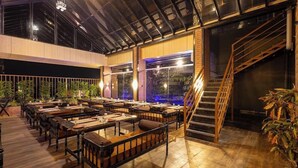 A spacious indoor dining area with wooden tables and benches, large windows, and a staircase. - Hotel Money Plant (Chhatrapati Sambhajinagar)